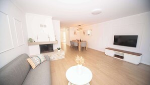 Un salon moderne comprenant un canapé, une table basse ronde, une cheminée, un coin repas avec des chaises et un téléviseur fixé au mur.