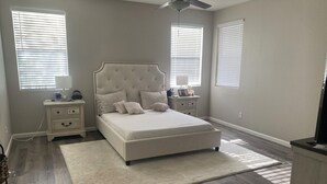 A bedroom with a large bed, nightstands, a ceiling fan, and a view of the outside through the windows. - Stunning Avondale Home! (Avondale)