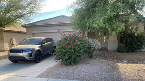 A residential driveway with a Range Rover parked on the left. There is a well-maintained garden with flowering bushes and a small tree. - Stunning Avondale Home! (Avondale)