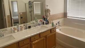 A bathroom with a large mirror, two sinks, a bathtub, and a window with blinds. - Stunning Avondale Home! (Avondale)