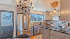A modern kitchen with stainless steel appliances, a chandelier, and pendant lights. - Large Family-Friendly 3BE Home | Easy Access to QE2 (Airdrie)