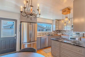 A modern kitchen with stainless steel appliances, a chandelier, and pendant lights.