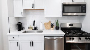 Una cocina moderna con armarios blancos, un microondas de acero inoxidable, una estufa a gas y un lavavajillas.
