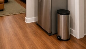 Un refrigerador de acero inoxidable en una cocina moderna, con un bote de basura a su lado.