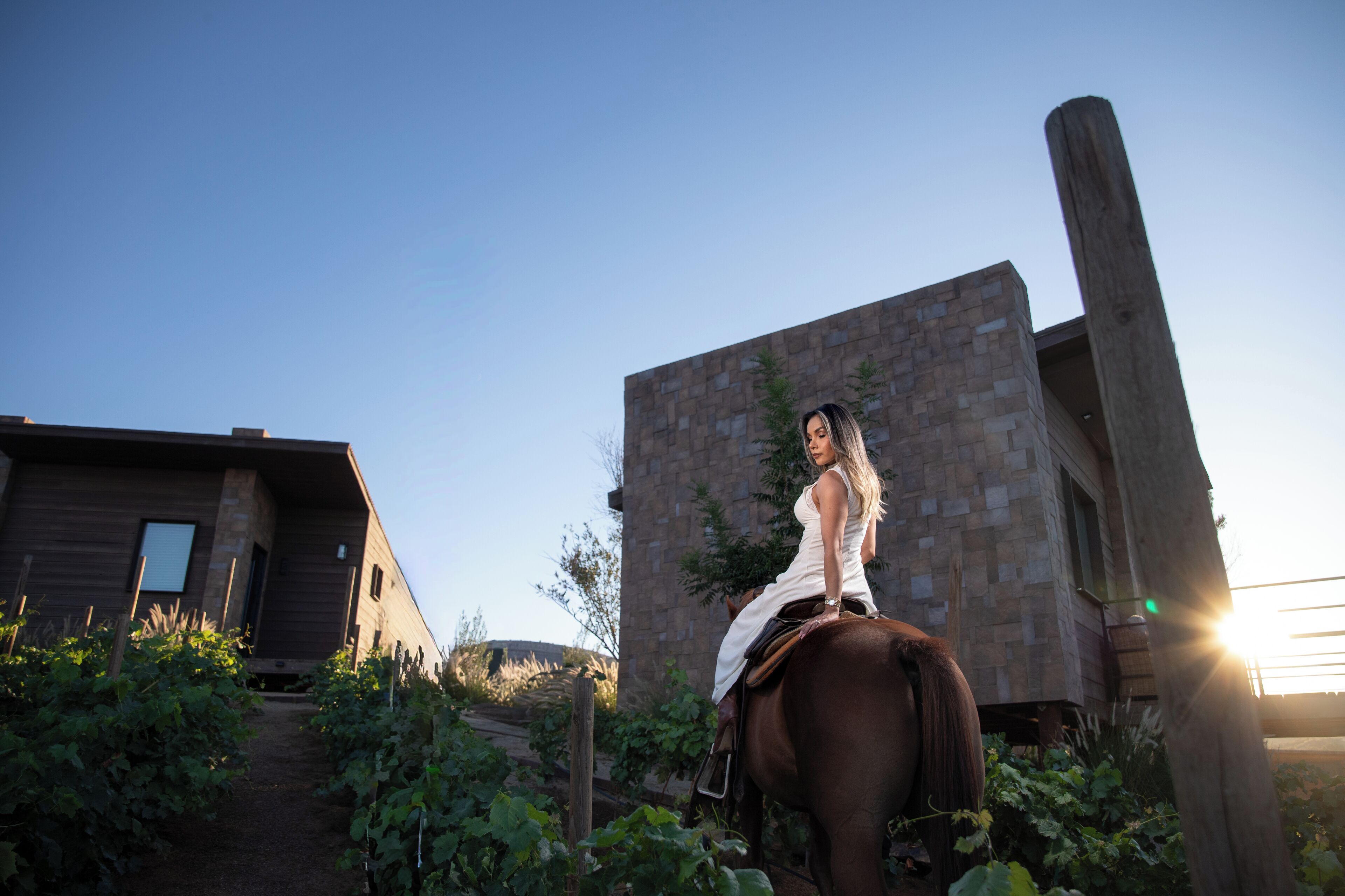A woman riding a horse in front of a rustic building with a clear sky.