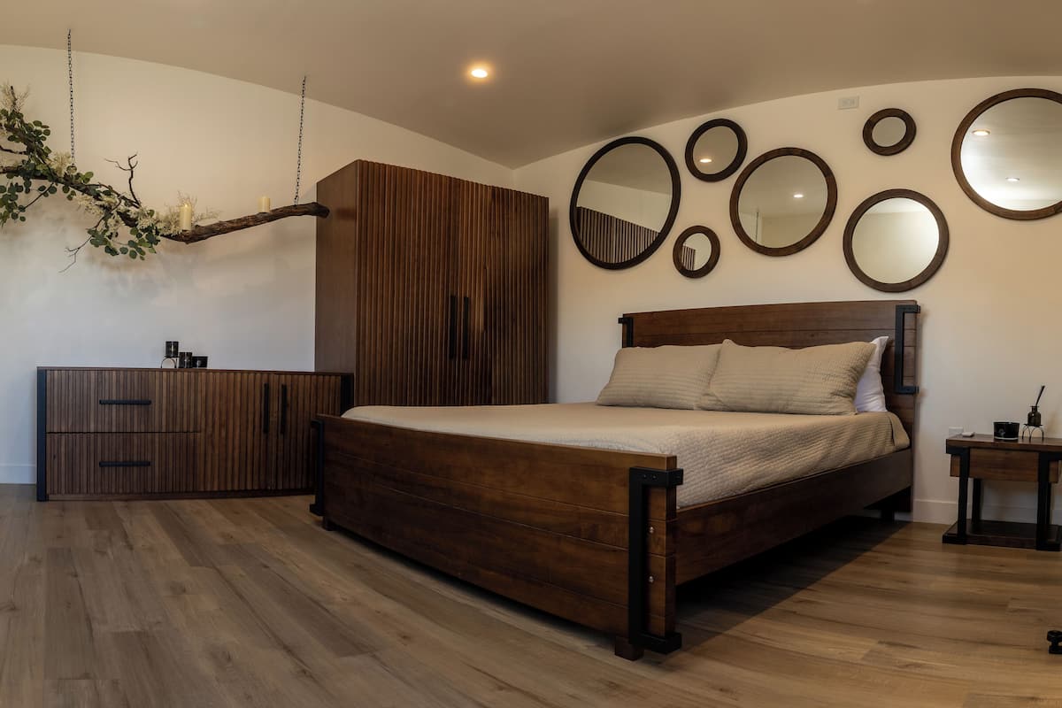 A bedroom with a wooden bed, a wardrobe, and multiple wall-mounted mirrors.