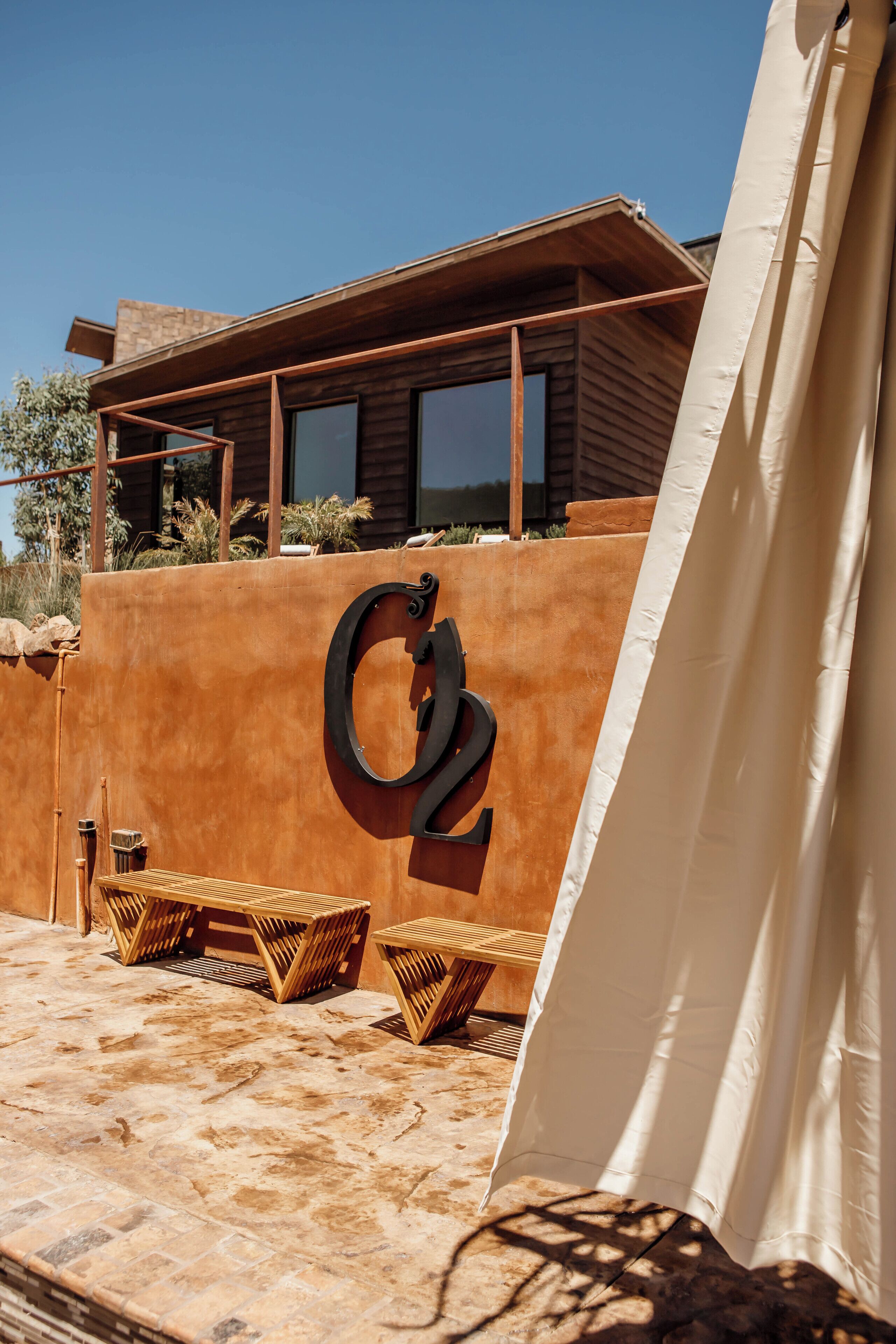 Un espace extérieur moderne aménagé avec des sièges, un grand panneau portant le chiffre «  02 », du mobilier en bois et une tente.