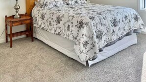 Un dormitorio con cabecera de madera, colcha estampada con motivos florales, dos lámparas de noche y ventana con vistas.