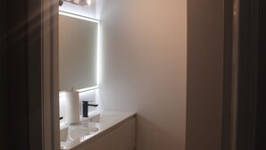 Un baño moderno con un tocador blanco, un espejo grande y una lámpara sobre el espejo.
