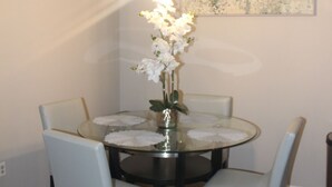 Una mesa redonda para comer con seis sillas, un florero con flores blancas e una lámpara colgante.