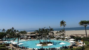 Un área de piscina en un resort, con varias piscinas, sillas de descanso, sombrillas y palmeras.