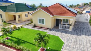 A residential house with a green lawn, a red roof, and solar panels.
