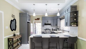 A modern kitchen with grey cabinets, a central island with bar stools, pendant lighting, and a built-in oven.