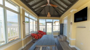 A covered patio with a wooden table and benches, large windows, and a ceiling fan.