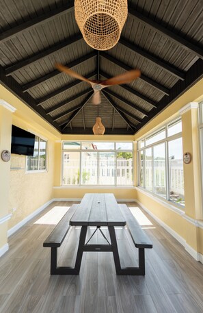 A covered patio area with a picnic table, ceiling fan, and large windows. - Clare's Manor – 2BR Villa with Mini Golf Course in Ocho Rios (Ocho Rios)
