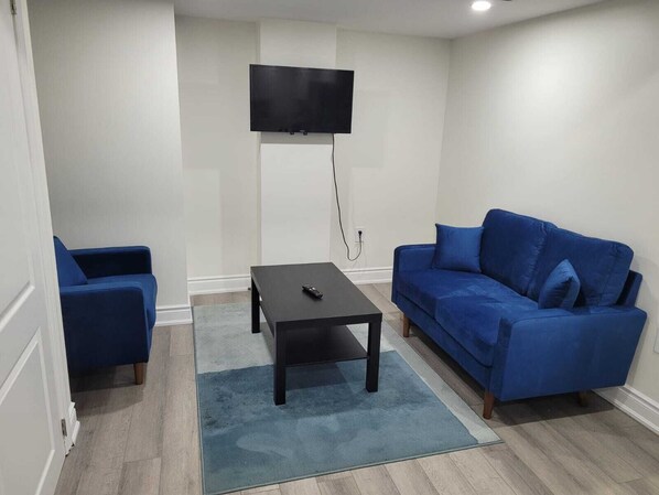 Un salon avec un téléviseur fixé au mur, un canapé bleu, un fauteuil assorti et une petite table basse.