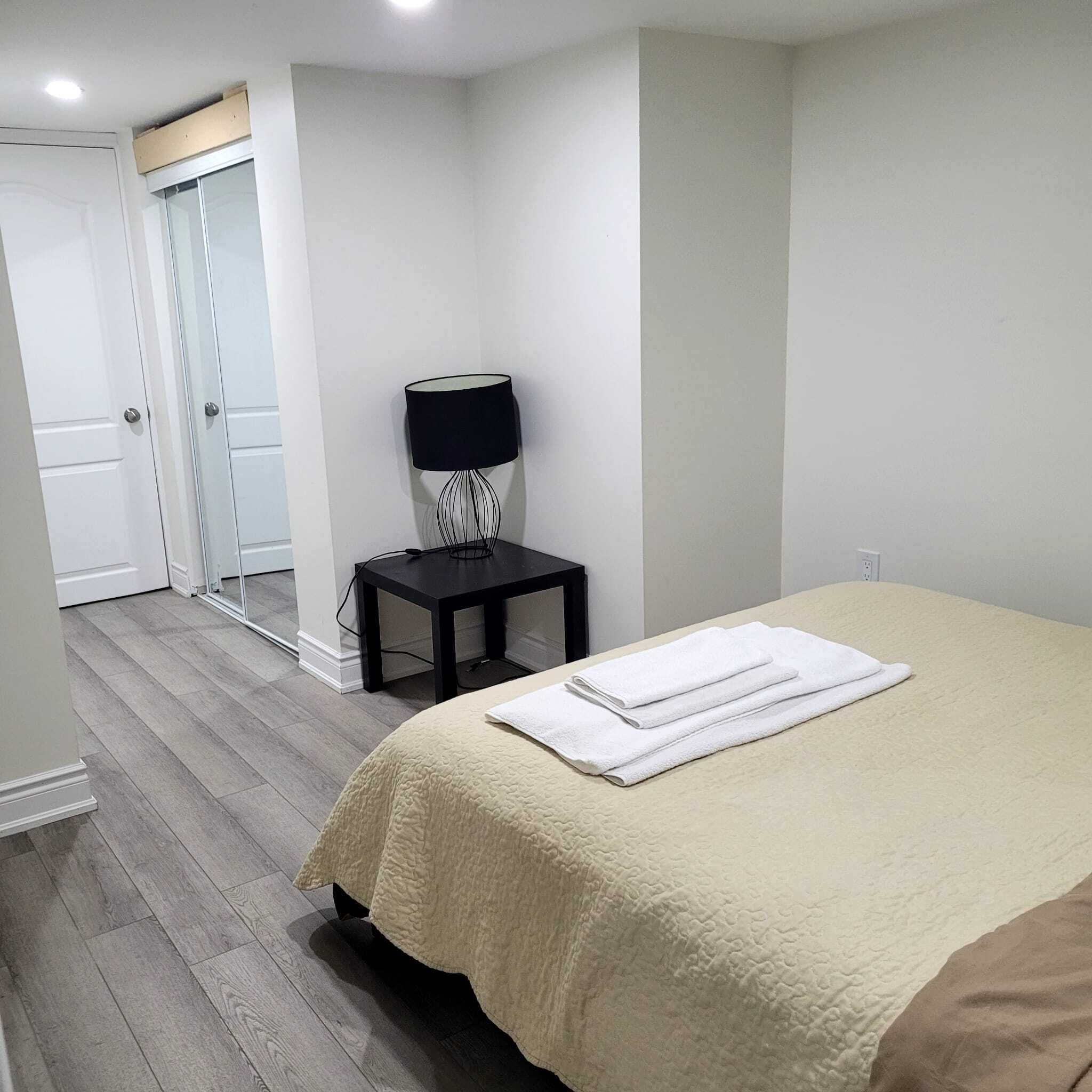 Une chambre à coucher comprenant un lit, une table de chevet, une lampe et une porte donnant sur une autre pièce.