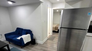 A compact living space with a kitchenette, a blue sofa, and a refrigerator. - Brand new 2-bedroom Apartment with  AC/Heat in Brampton (Brampton)