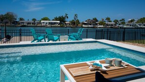 Une piscine entourée de chaises turquoise et d’une terrasse en bois.