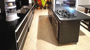 A modern kitchen with a central island, black countertops, and a colorful corn mural on the wall. - Hostal Galería de la Montaña (Medellín)