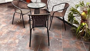 A small outdoor patio with a round table and four wicker chairs, a hammock, and a potted plant. - Hostal Galería de la Montaña (Medellín)