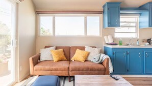 Una sala de estar con un sofá marrón, dos cojines amarillos, un reposapiés azul y una mesa de centro de madera.