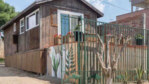 Una casa de madera con puerta verde, cercado metálico con diseños de plantas y un pequeño jardín.