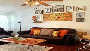 A living room with a ceiling fan, a sofa, a coffee table, and a wall with framed artwork.