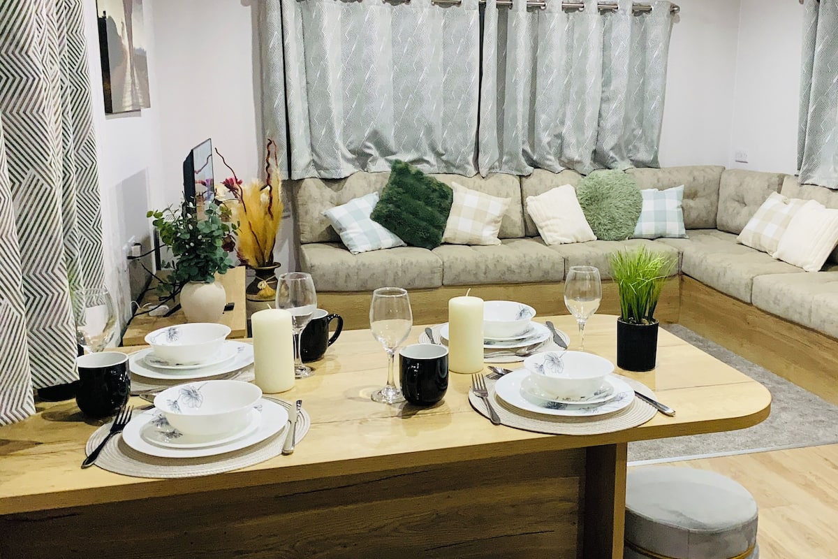A dining area with a wooden table set for four, surrounded by a beige sofa with patterned cushions.