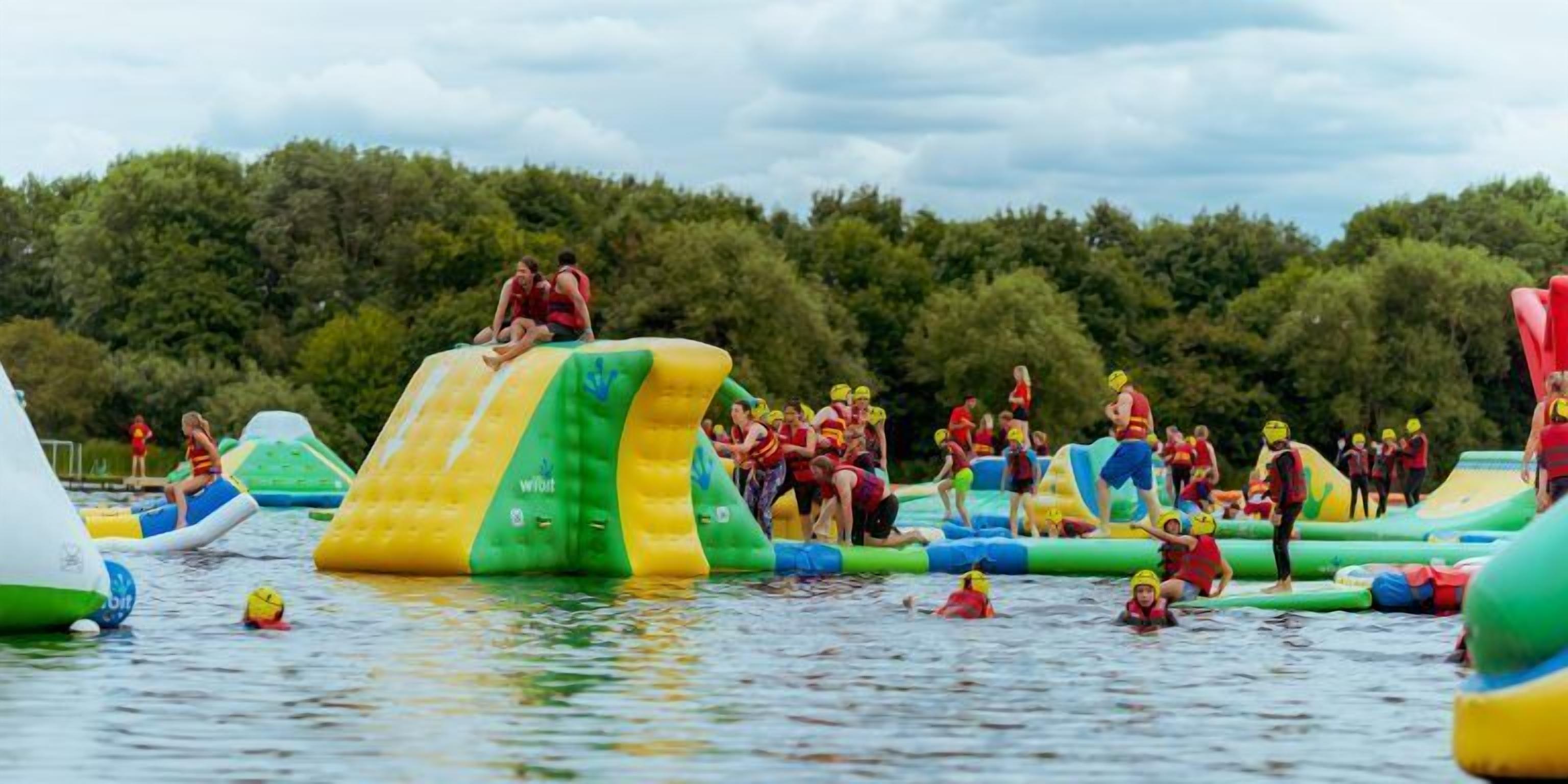 Een recreatiegebied met wateractiviteiten, opblaasbare attracties en mensen die waterspelletjes spelen.