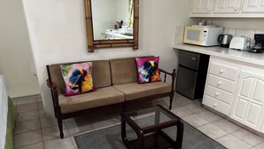 A living room with a sofa, a glass coffee table, and a kitchen area with appliances. - Villa Mia Apartments Studio #3 (Oistins)