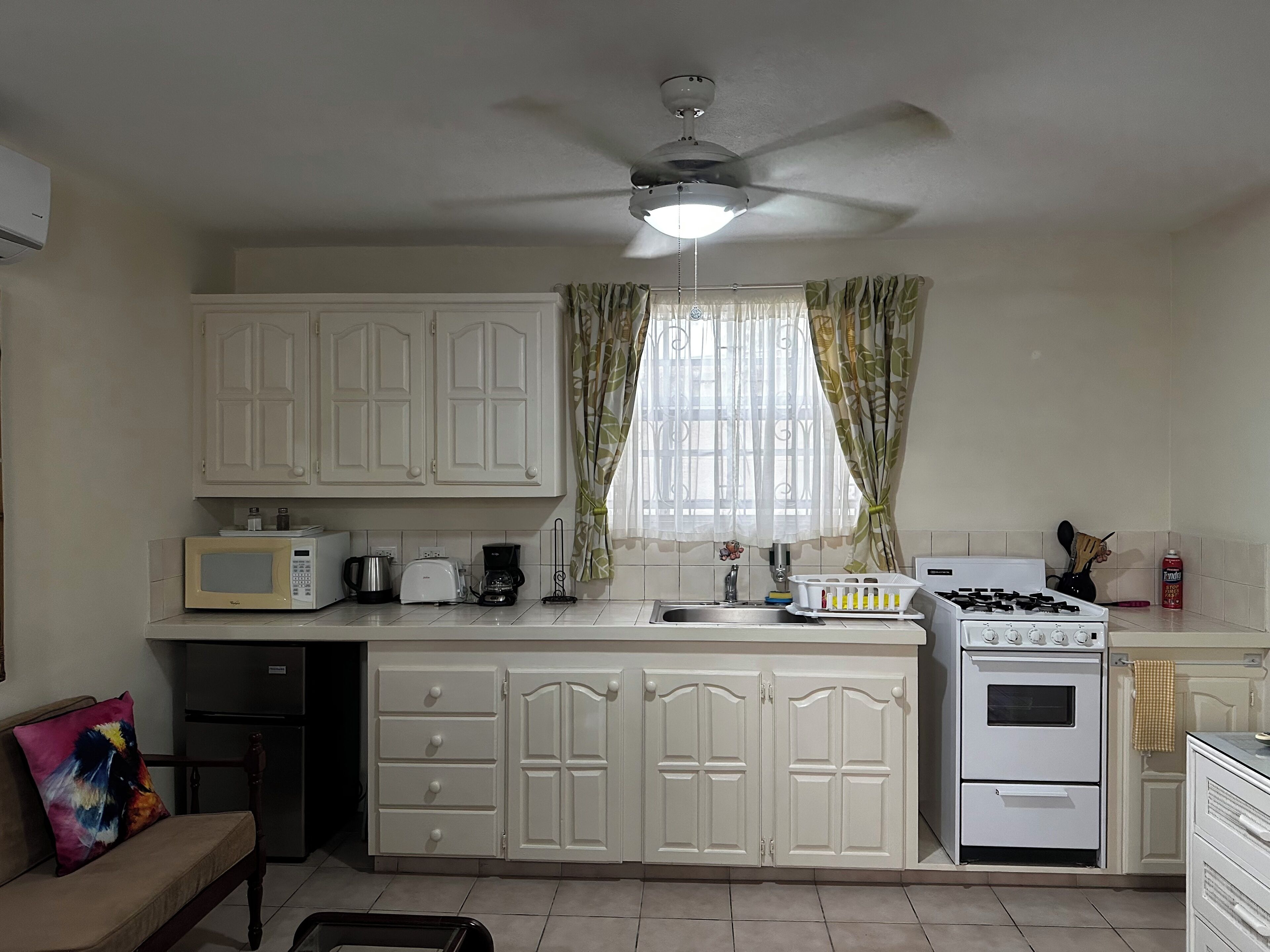 A compact kitchen with white cabinets, a microwave, a coffee maker, a toaster, a sink, and a stove.