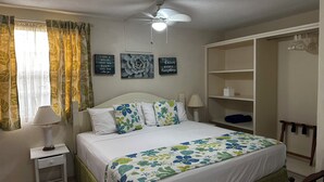 A neatly arranged bedroom with a bed, a nightstand, a lamp, a ceiling fan, and a wardrobe. - Villa Mia Apartments Studio #3 (Oistins)