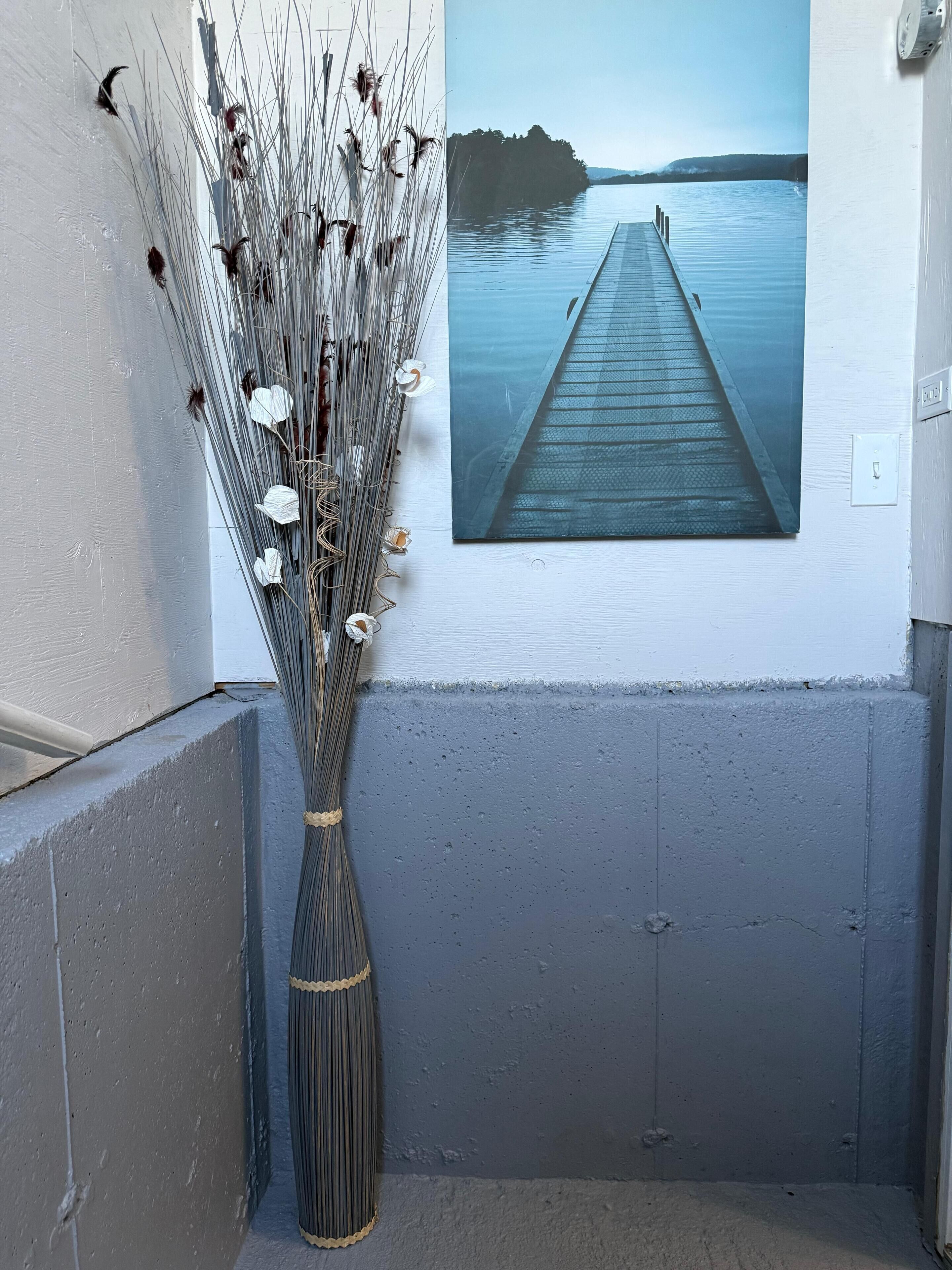A hallway with a concrete floor, a white wall, and a framed photograph of a pier extending into a calm body of water.