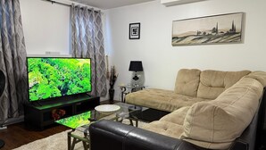 Una sala de estar con un televisor de pantalla plana, un sofá color beige, una mesa de centro, una lámpara y un cuadro en la pared.