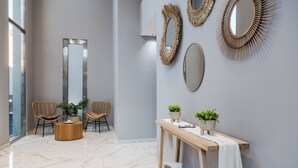 Un hall d’entrée moderne avec un sol en marbre, deux fauteuils en osier, une console en bois agrémentée de plantes et des miroirs décoratifs.