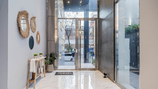 Un hall d’entrée moderne avec un sol en marbre, un comptoir d’accueil en bois et une porte en verre donnant sur l’extérieur.