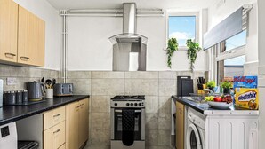 Una cucina compatta con piano cottura, forno e lavatrice, pensili in legno e una finestra con piante.