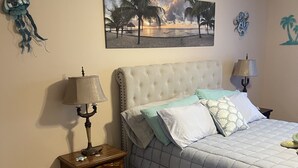 Een slaapkamer met een bed, nachtkastjes, een wandlamp en een schilderij met een strandthema.