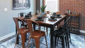 A dining area with a brick wall, a cityscape painting, and a modern chandelier. - Themed Home | Walk to Downtown | Arcade | Fire Pit (Indianapolis)