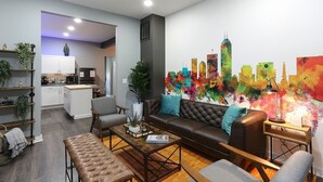 A modern living room with a brown leather sofa, a wooden coffee table, and a grey armchair. There is a colorful abstract painting on the wall and a small table with a lamp. - Themed Home | Walk to Downtown | Arcade | Fire Pit (Indianapolis)