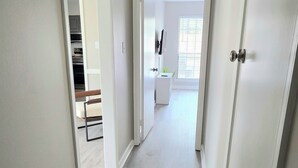 A hallway with a light-colored wooden floor, white walls, and a door on the right.