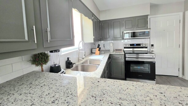 A modern kitchen with grey cabinets, a granite countertop, a built-in microwave, and a stainless steel oven.