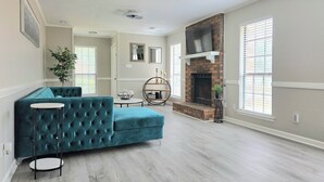 A living room with a teal sectional sofa, a fireplace, and a large window.