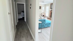 A hallway with a wooden floor leading to a bedroom with a bed and a bathroom.