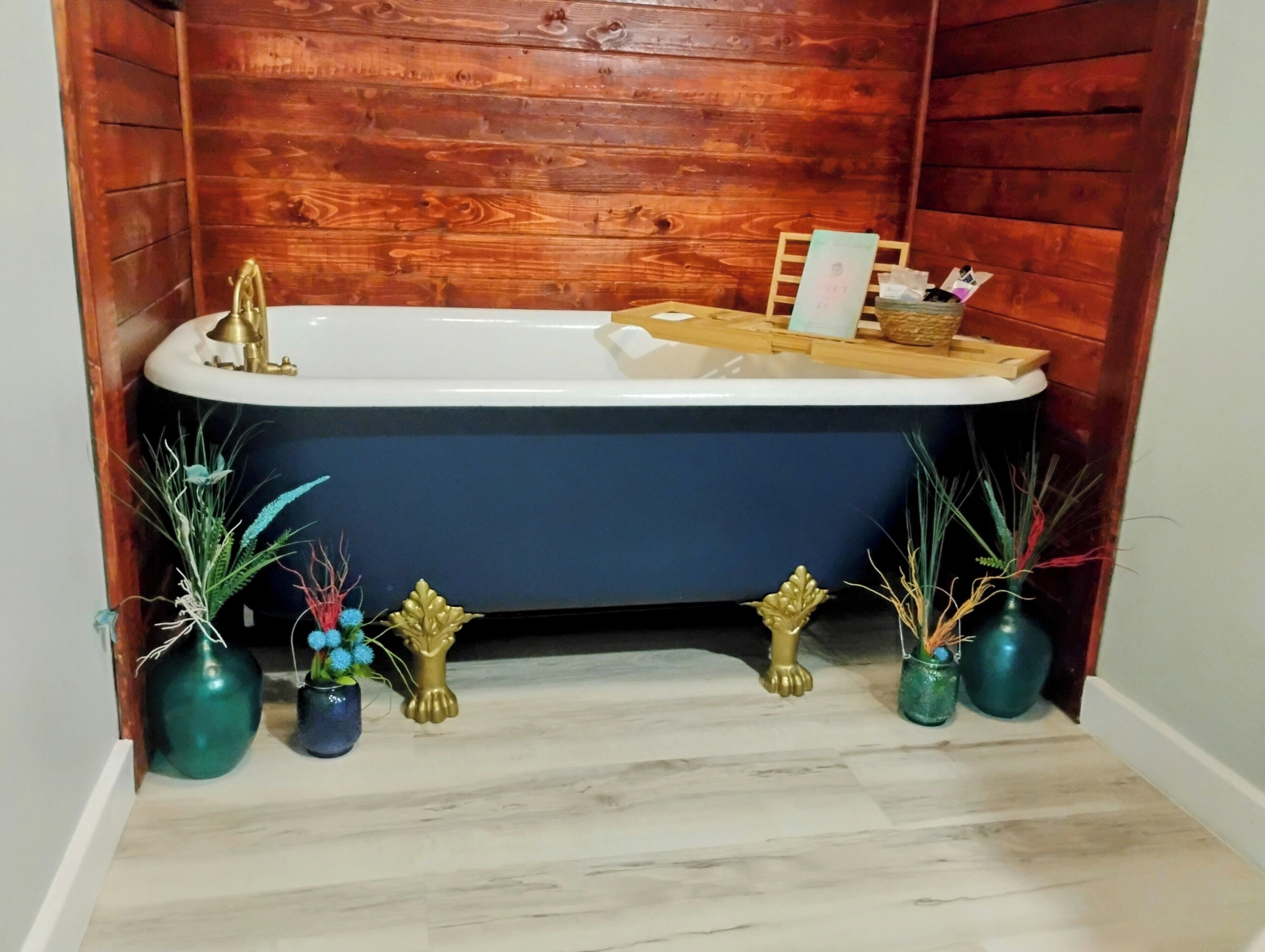 A bathroom with a bathtub, wooden panel walls, and decorative vases on the floor.