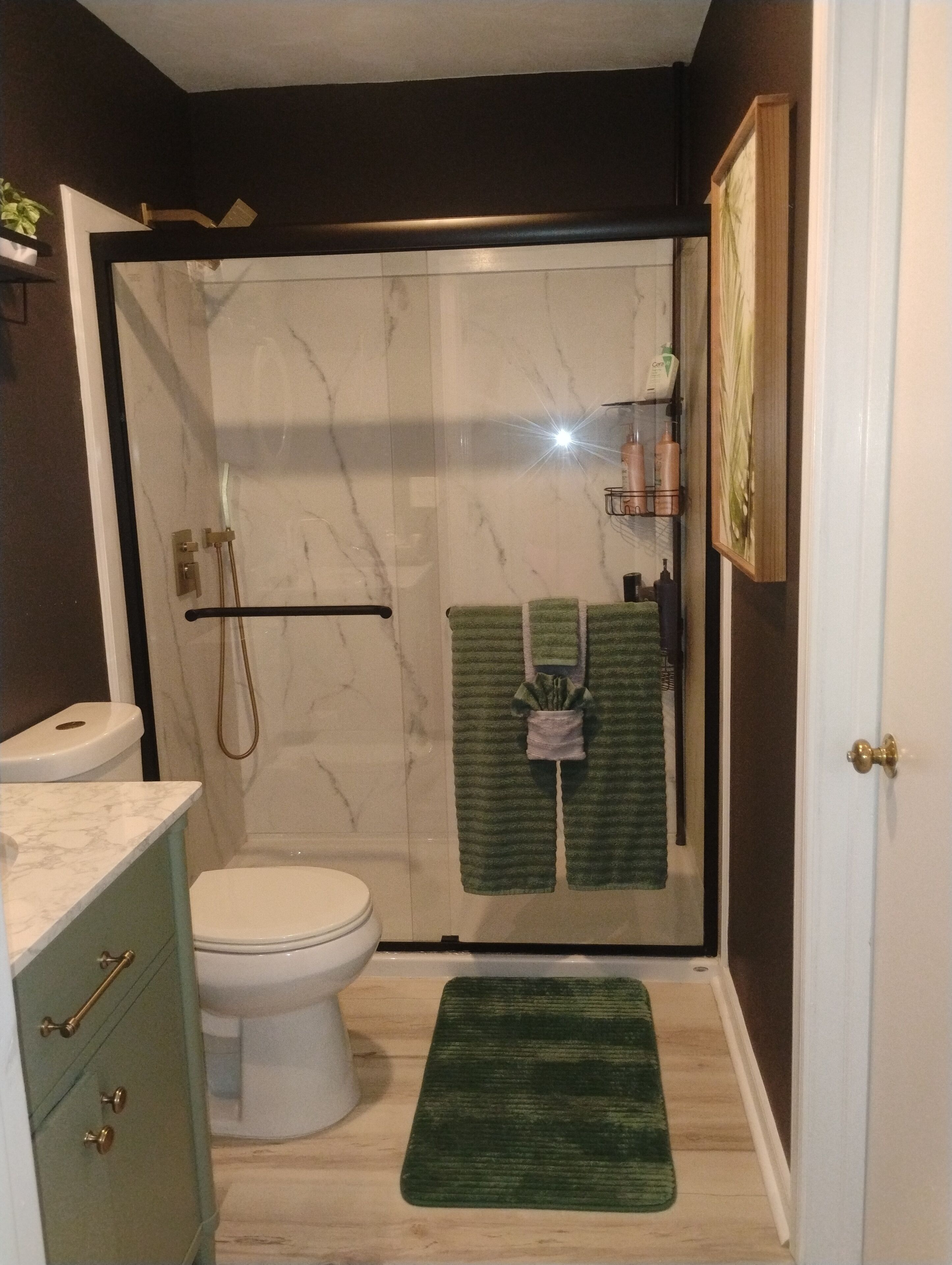 A bathroom with a shower, toilet, and a green towel hanging on the wall.