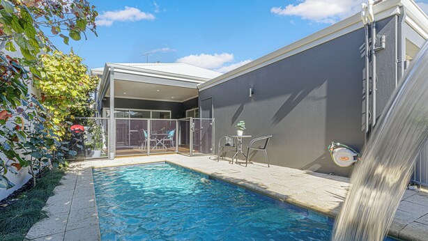 A swimming pool with a waterfall feature, surrounded by a covered patio area with seating.