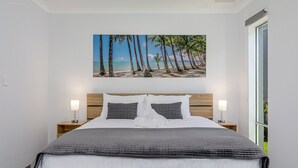 Une chambre à coucher comprenant un lit, deux tables de chevet, une tête de lit et un tableau représentant une scène de plage, accroché au mur.