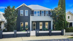 A modern two-story house with a balcony, a gated entrance, and a well-maintained garden.